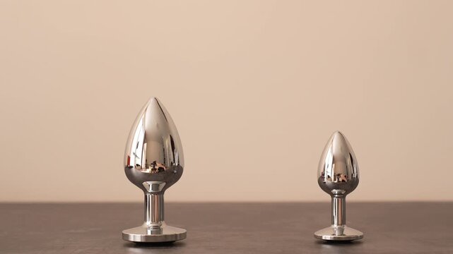 Woman in black transparent glove takes metal anal plug with black crystal from shelf. BDSM erotic set. Adult toys.