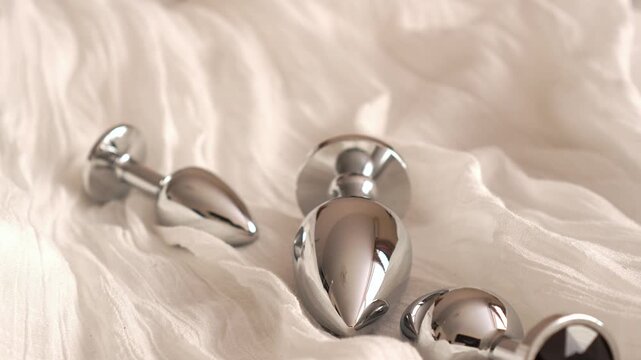 Metal butt plugs of various sizes with black rhinestones fall onto the bed. BDSM erotic set. Adult toys.