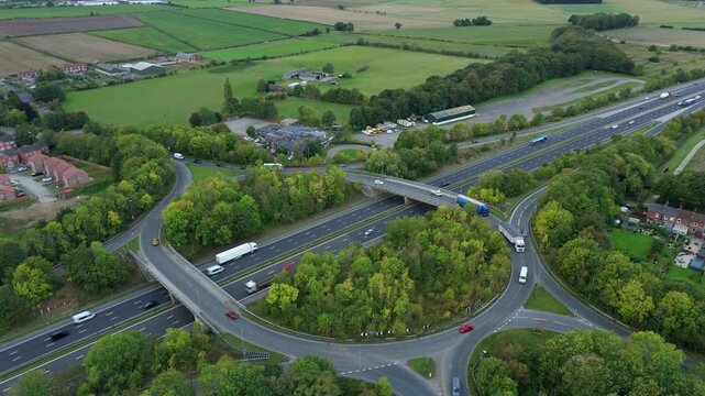 Aerial view of a highway interchange with a roundabout surrounded by lush green trees and the distant fields, Goole, England, United Kingdom.