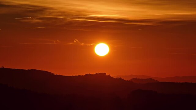 Timelapse of the sun setting over mountain ridge with warm orange sky and fading light at dusk