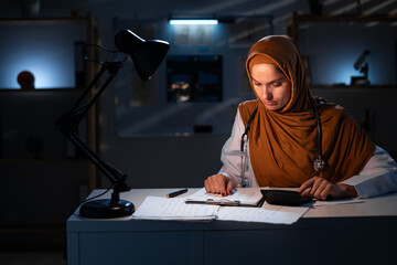 Muslim female Doctor calculate medical fee costs working on night shift in hospital. practitioner use calculator.