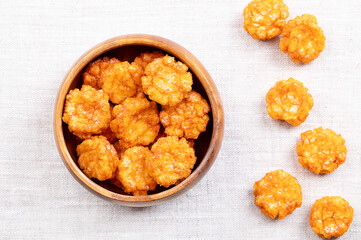 Thai chili rice crackers in a wooden bowl on linen fabric. Hot, sweet and spicy crispies, a snack made of rice, seasoned with chili powder and flavored with soy sauce. Close-up from above, food photo.