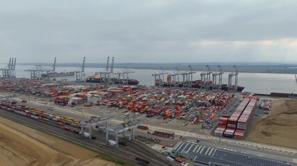 London, United Kingdom - 11 October 2025: Aerial view of the London Gateway port, a symphony of red containers, cranes, and ships against the grey sky.