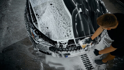 Worker washing car hood with sponge during foam cleaning process. Concept of car wash detailing...