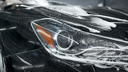 Close-up of car headlight covered with foam during washing process. Concept of automotive detailing, clarity preservation, marketing for car cleaning services.