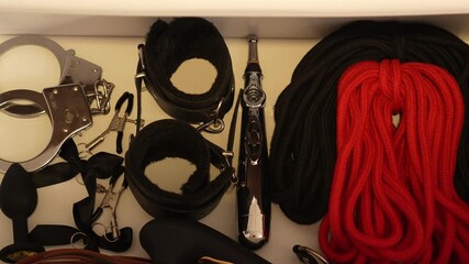 Woman in transparent glove opens bedside table with adult toys. BDSM set. Handcuffs, ropes, gag, whip, vibrator, butt plug, clamps, current.