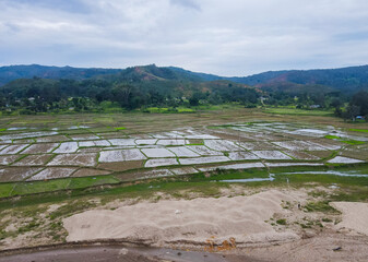 Aerial landscape of land use contrast in Aileu, Timor-Leste. A sand quarry sits beside rice paddies and forest, with distant mountains framing the scene.