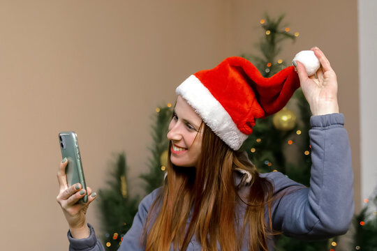 Happy woman against Christmas tree at home using smartphone app call virtual chat.beautiful girl in santa claus hat online video.Merry New Year,Happy Holidays Celebration.