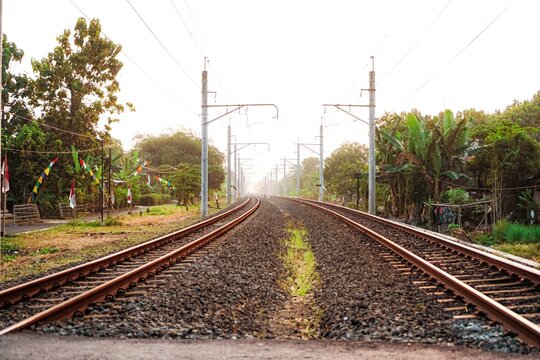A straight-on, low-angle view of two parallel train tracks extending into the distance through a rural area on a sunny day.