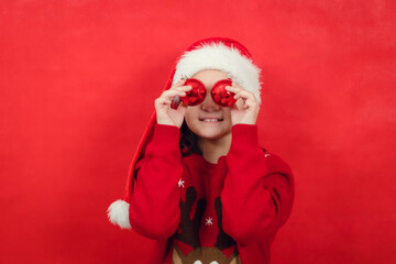 Close-up portrait of teenage girl, near eyes holding Christmas balls, red background, copy space