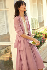 Graceful woman in a light pink outfit holding fruit in a bright outdoor setting.