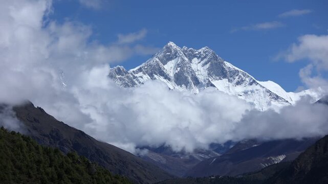 Magnificent view of the Kanchenjunga Region in Nepal, with snow-covered Himalayan peaks emerging through drifting clouds, framed by lush valleys and a clear blue sky, evoking awe and tranquility.