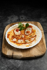 Close-up of Halloween-themed pizza with smiling face made from vegetables and cheese on white plate over wooden board, top view food photography