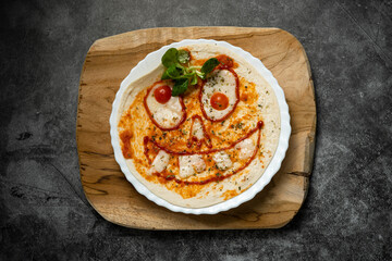 Close-up of Halloween-themed pizza with smiling face made from vegetables and cheese on white plate over wooden board, top view food photography