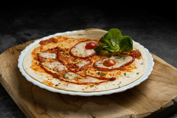 Close-up of Halloween-themed pizza with smiling face made from vegetables and cheese on white plate over wooden board, top view food photography