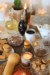 Lit candles, cookies, chocolate, nuts, tea, wine, pumpkins, books, reading glasses and autumn leaves on the table. Autumnal hygge at home. Selective focus.