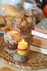 Lit candles, cookies, chocolate, nuts, tea, wine, pumpkins, books, reading glasses and autumn leaves on the table. Autumnal hygge at home. Selective focus.