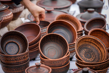 Handcrafted ceramic bowls with rustic brown glaze and carved patterns displayed at an outdoor market, artisan selecting pottery for sale, traditional craftsmanship.