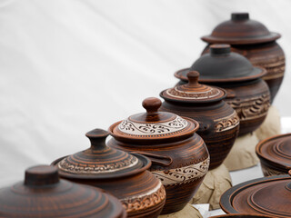 Handmade traditional ceramic jars with ornate carved patterns and lids, arranged in a rustic row on a white background, perfect for home decor or cultural themes.