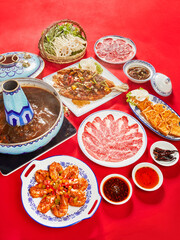 Traditional Chinese Hot Pot with Sliced Beef, Vegetables, and Dipping Sauces on Red Table