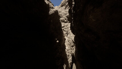 A breathtaking view of a narrow canyon formed by towering rock walls. The sunlight illuminates the rocky textures while a clear blue sky creates a vivid contrast above, making the scene captivating.