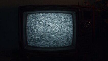 Flickering CRT television set displaying static in dark study, with rotary knob and houseplant