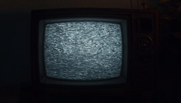 Flickering CRT television set displaying static in dark study, with rotary knob and houseplant - Powered by Adobe