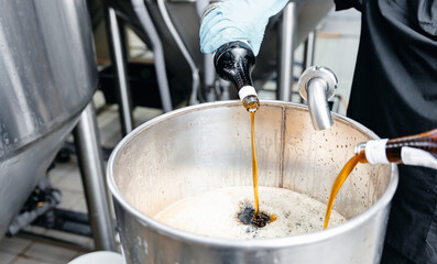 Brewing process in beer factory with bottles pouring into metallic tank