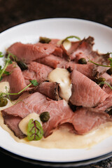 Delicious roast beef with creamy sauce and capers on white plate