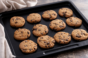 Baked chocolate chip cookies on a black baking tray on wooden table