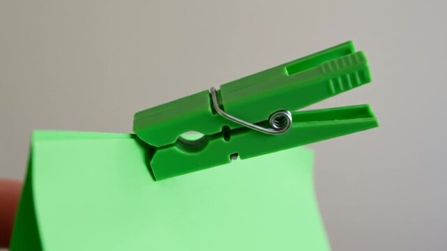A vibrant green clothespin holds together a stack of bright green sticky notes against a neutral backdrop. Spring hinge is metallic