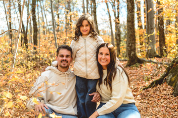 Fototapeta premium Beautiful young family having great time in autumn forest with little daughter