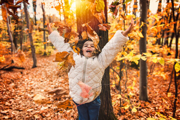 adorable happy girl playing with fallen leaves in autumn park