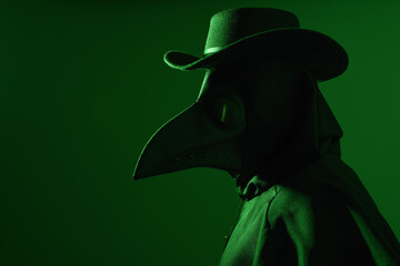 close up portrait of Plague Doctor Halloween Costume with Glowing Green background, Gothic Character in Black Cloak, bird Mask and top hat. Dark Fantasy Horror Scene with silhouette profile figure.