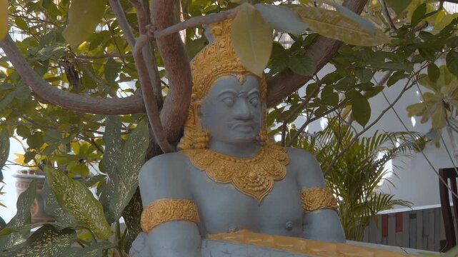 A statue of a Khmer hermit with golden crown and ornaments meditating under the tree. Shot in motion 