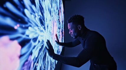 African American man interacts with glowing digital screen displaying light bursts. Futuristic touch interface technology in blue and pink hues. Innovative virtual display footage - Powered by Adobe