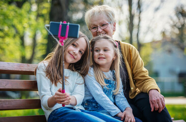 Happy grandmother taking selfie with granddaughter's on park bench