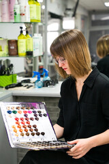 A young woman chooses a hair dye color while sitting in a hairdressing salon. Dyeing, changing hair colour, safe haircare concept. Selective focus.
