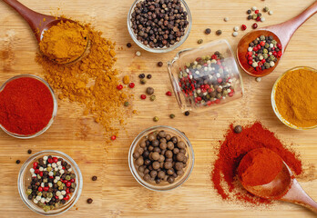 Aromatic spices in wooden spoons and transparent bowls on wooden background. Culinary inspiration.