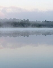 Fototapeta premium Soft mist over calm lake during sunrise showing peaceful natural reflection