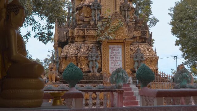 Massive golden stupa with statues of Yakshas demon guardians on its levels stand in the temple grounds of Wat Svay Romeat Pagoda in Siem Reap, Cambodia. Shot in motion