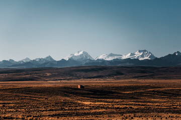 Obraz premium arid landscape in bolivia with snowy peaks in the background and a small house
