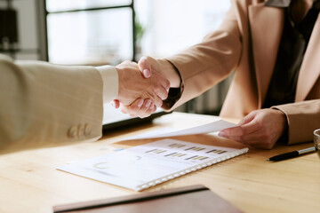 Caucasian middle aged man shaking hands with Caucasian young adult woman during business meeting, holding contract and discussing financial documents on office desk