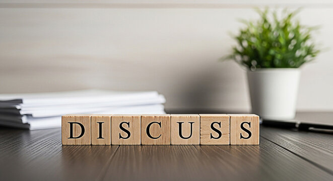 Wooden blocks spelling "discuss" sit on a desk near paperwork and a plant promoting communication and collaboration in the workplace
