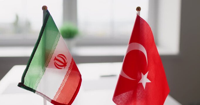 Diplomacy flags signal negotiation during bilateral meeting. Iran and Turkey mini desk banners on a conference table suggest agreement and partnership. Concept: diplomatic talks and cooperation.