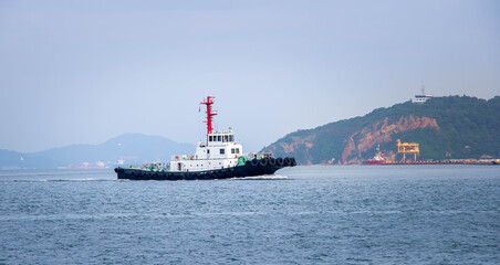 Assistance Tug Vessel Cruising Near a Hilly Coastline and Port Facilities