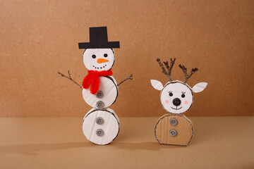 Cardboard snowman and reindeer handmade Christmas crafts with buttons, scarf, hat, and twig antlers on brown background. DIY winter decoration project. Studio composition for greeting card, poster © Elena