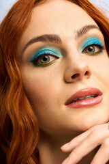 Fototapeta premium Vibrant redhead with bold makeup poses elegantly in a bright studio setting