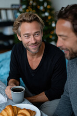 Two men share a delightful moment over coffee and croissants, capturing a relationship full of laughter and warmth in a cozy, festive atmosphere during the holidays.
