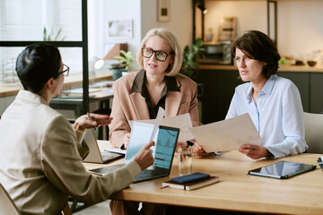 Three Caucasian middle aged women sitting at table discussing business documents and analyzing...